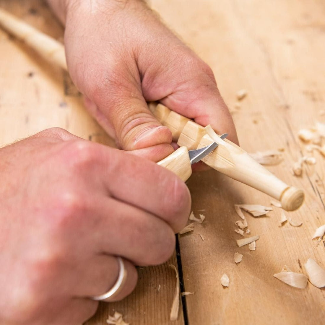 the carver is carving a stick with the smallest detail knife on a bench.