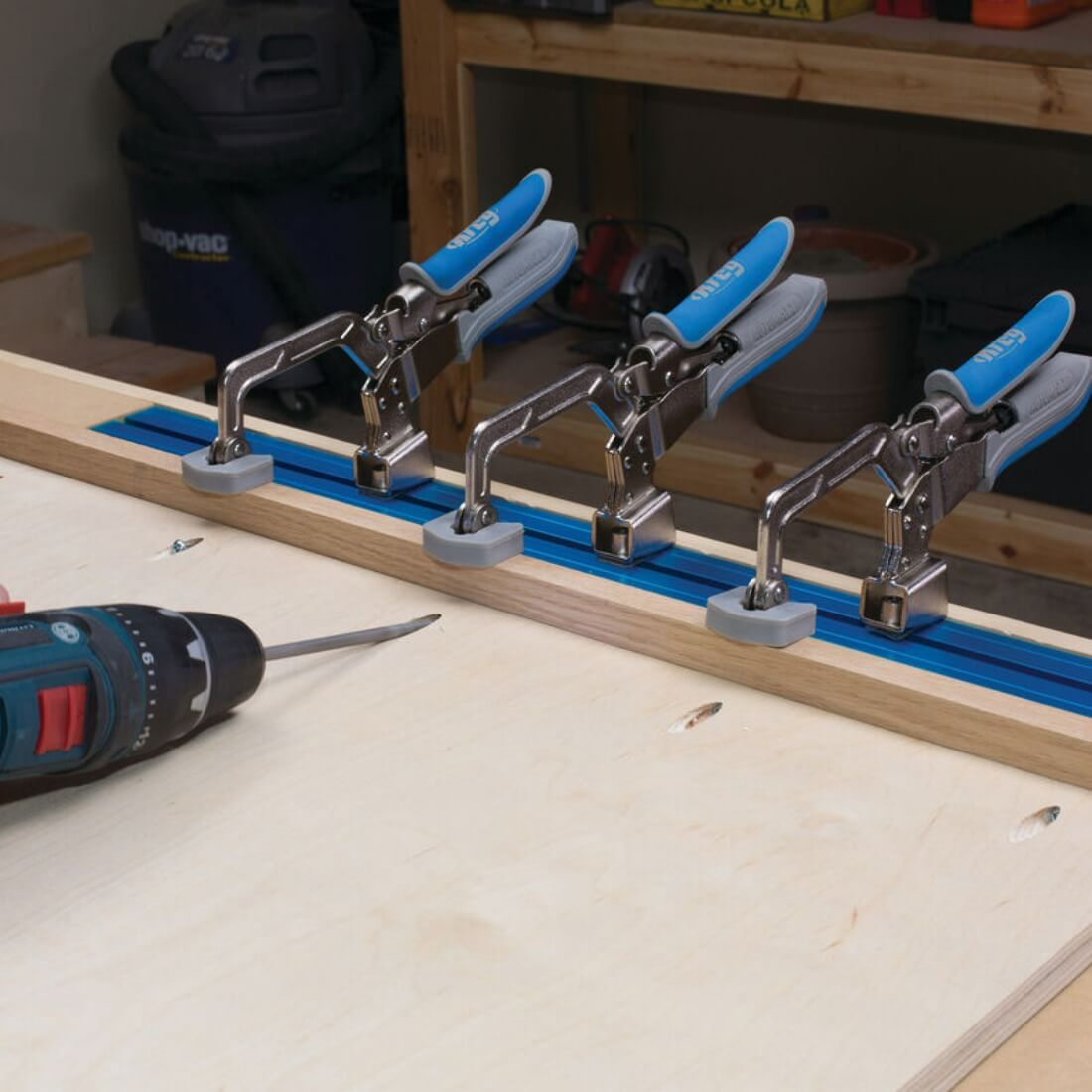 Kreg Automaxx 3 inch Bench Clamps in a row of three fitted to bench rail holding a wooden frame with being screwing pocketed sheet to a wooden baton 