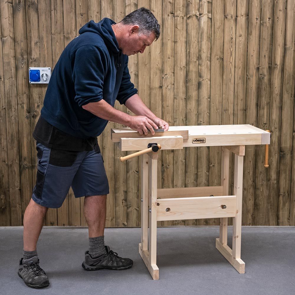 adult using the dual height Sjobergs Adult/Kids Workbench. Block of wood has been placed in the side vice and is being planed.