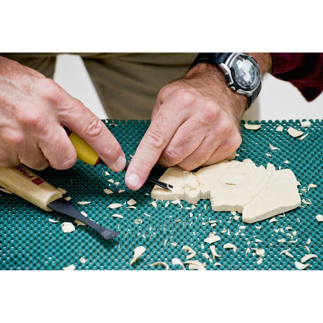 picture is showing a carver carving a flat piece of basswood with one of the gouges from the SK108 set. Wood is placed on a non slip rubber matt