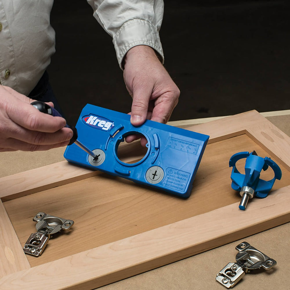picture showing user making adjustment setting for drilling cabinet door. Two kitchen type hinges on show and the forstner bit installed in it's holder.